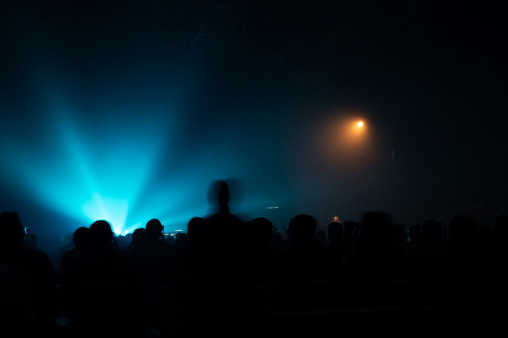 A concert crowd facing a stage lit in cyan